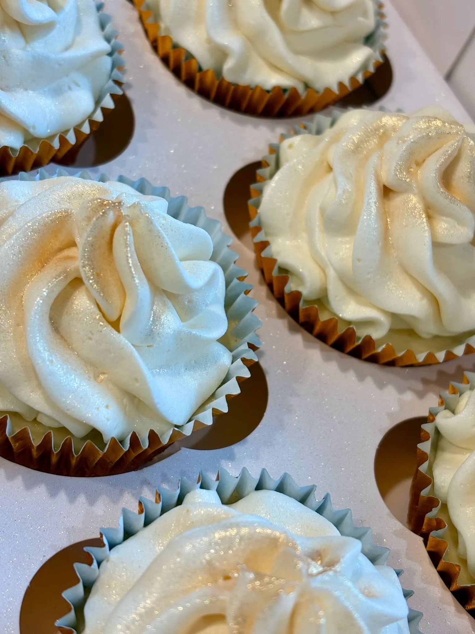 Close-up of cream cheesecake cupcake frosting swirls with gold and silver edible glitter on gold foil cases